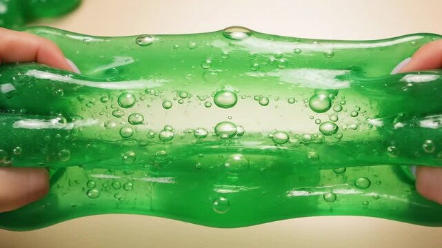 Vibrant green slime being stretched and squished with hands on a light
