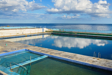 Outdoor seawater training pools for a diving school reflecting a cloudy blue sky by the sea, used for scuba diver education and water sports activities.