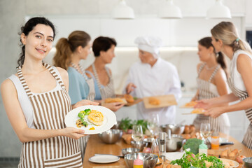 Young woman poses with prepared chicken dish at cooking master class