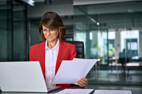 Focused latin business woman accountant working on laptop computer reading financial contract document in office workplace. Mature manager businesswoman specialist doing paperwork using pc. Copy space
