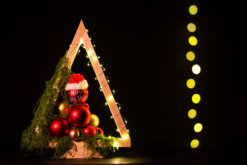 Modern DIY wooden Christmas tree with LED lights, moss, red balls and ornaments on a neutral background