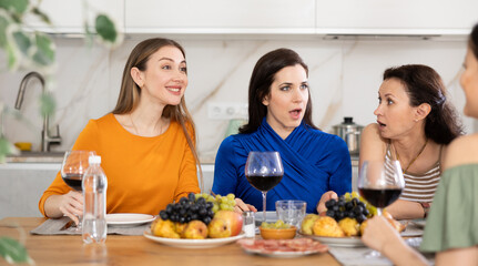 Casual evening where group of cheerful carefree besties sharing wine, dining together, and chatting in cozy home kitchen ..