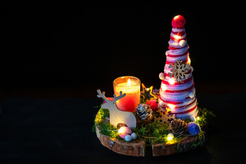 A cozy, dimly lit Christmas centerpiece featuring a candle, a festive yarn-wrapped tree, and wooden reindeer on a moss-covered log slice.
