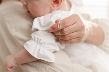Sacrament of baptism. Woman holding little baby and gold cross indoors, closeup