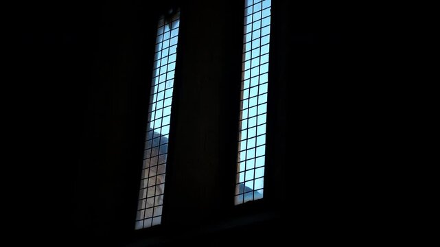 Dark room window light revealing building exterior. Sunlight gradually illuminates the exterior of a historic building, viewed from inside a dark, shadowed room through two tall, narrow windows
