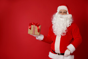 Santa Claus with Christmas gift on red background, space for text