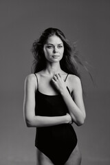 Fototapeta premium Black and white portrait of a young woman in a simple black bodysuit with calm expression and windblown hair.