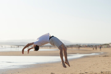Young man performing backflip on sandy beach