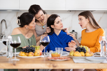 Group of empathetic and caring female friends gathering around table to console upset bestie during friendly get-together with wine at home..