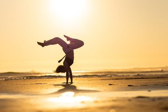 Capoeirista performing handstand on beach during sunset