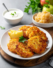 A white plate features several golden Potato Latkes served with a side of cold applesauce and thick cream.