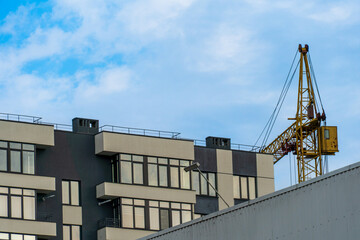 A crane is on top of a building. The crane is yellow and has a yellow cab. The building is gray and has windows
