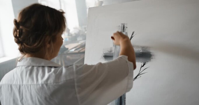 Female artist painting abstract cross on canvas