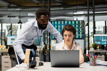 Fototapeta premium Multiethnic coworkers discussing projects at desk. Black male executive and female employee using laptop on table to analyze reports, track statistics and plan corporate growth strategies.