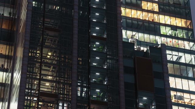 Timelapse modern office building at night, glass elevators moving up and down inside the structure. Illuminated windows reveal vertical motion, business activity, nonstop rhythm of downtown life