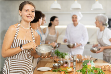 Young woman learns to prepare dish at cooking master class