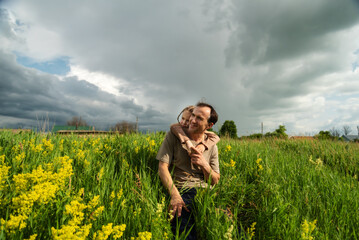 Caucasian adult male with child embraced in wildflower field under cloudy sky