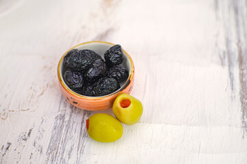 Gourmet black olives are served in a small bowl alongside two vibrant green varieties. Showcasing healthy appetizer ingredients on a white wooden surface. Ideal for recipe promotion. Selective focus.