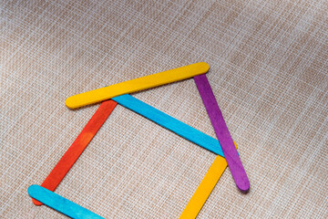 Multicolored craft sticks are arranged in an unstable outline of a basic house shape. Symbolizing challenges in property construction or home ownership. Ideal for finance concepts.