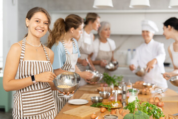 Young woman holding bowl in her hands posing surrounded by other members of cooking course