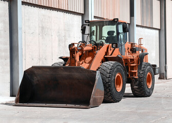 Front view of a powerful orange industrial wheel loader with a large bucket parked near a warehouse. Heavy machinery for construction and mining