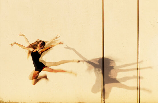 Artistic motion blur of a young girl leaping and dancing against a concrete wall