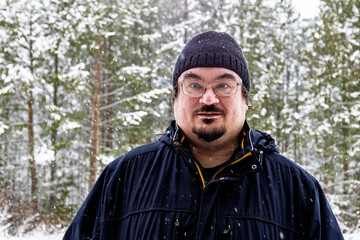 Startled anxious mood winter time dark knitted hat and dark jacket on white middle aged man standing in snowy forest with trees softly blurred behind.