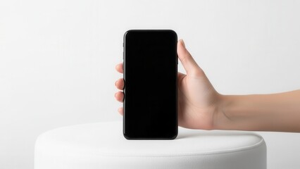 Minimalist composition with a hand holding a blank smartphone on a white pouf