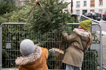 A brother and sister throw away Christmas trees behind the fence