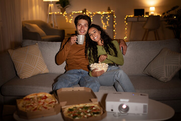 Two people relax on a couch at home, enjoying a fun evening together. They watch a movie from a...