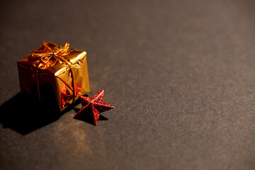 Minimal Christmas composition featuring a small golden gift box and a red glitter star on a dark...