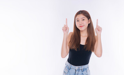Cheerful young Asian woman pointing index fingers up at empty copy space on white background. Beautiful happy female presenting product advertisement concept with smile.