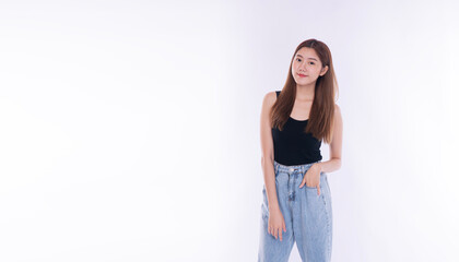 Casual young Asian woman standing with hand in pocket on white background. Relaxed beautiful female model in blue denim jeans smiling at camera with copy space