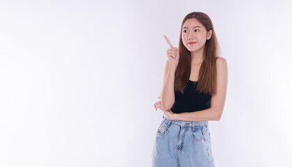 Thoughtful young Asian woman pointing finger at empty copy space on white background. Beautiful female model recommending product or getting new idea concept with smile.