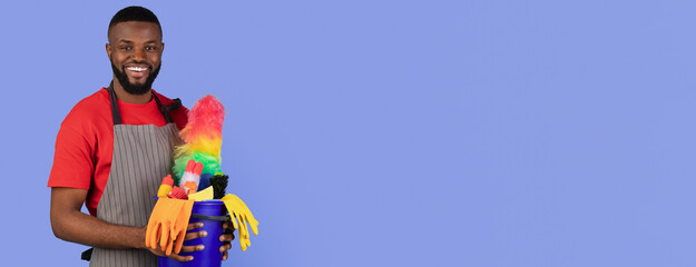 A man smiles while holding a container filled with various colorful cleaning supplies. He is wearing gloves and an apron, creating a vibrant and positive atmosphere for cleaning tasks.