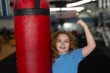 Child boxing practice at gym. Boy hitting punching bag. Young fighter in gloves. Sporty kid training hard. Strong child showing power. Youth workout in boxing ring. Active boy doing exercise.