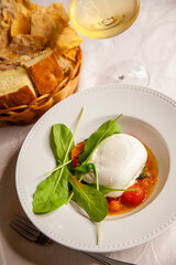 Italian cheese burrata with arugula and tomato close up and glass of white wine