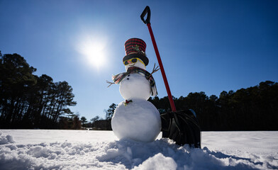 Obraz premium Snowman clearing snow with shovel. Winter scene with snowman with snow shovel and sled. Snow man ready to remove snow. Creative winter card with snowman. Snowman helping to clean the snowy road.