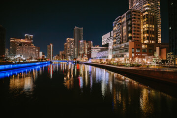 Obraz premium Wide Angle Night City Skyline Reflected in River with Blue Bridge Lighting and Skyscrapers