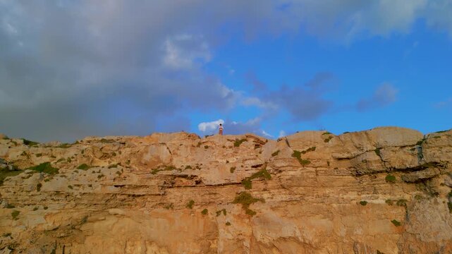Epic cliff traveler aerial reveal. 
Cinematic 4K drone vertical ascent over 
man standing on rocky mountain edge 
looking at isolated horizon landscape.
