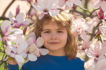 Fototapeta premium Spring fun for kids. Child play outdoors in a beautiful spring garden. Kid face in flowers. Adorable little kid in blooming cherry garden on beautiful spring day. Happy child during spring blossom.