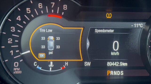 Car dashboard display shows tire pressure warning and speedometer at zero in a vehicle's instrument cluster.