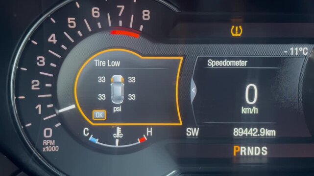Close-up of a car dashboard display indicating low tire pressure with various warning lights illuminated and speedometer details in view