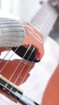 Vertical shot of woman playing acoustic guitar, practicing music at home, creative hobby lifestyle