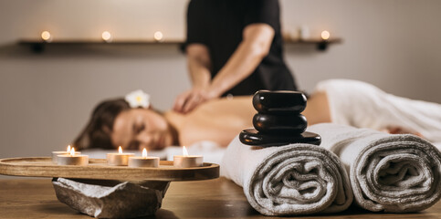 Relaxing spa scene with a woman receiving a soothing massage, surrounded by candles, towels, and...