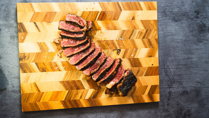 Thick rare smoked sirloin steak, sliced and elegantly arranged on a wooden board with Maldon salt....