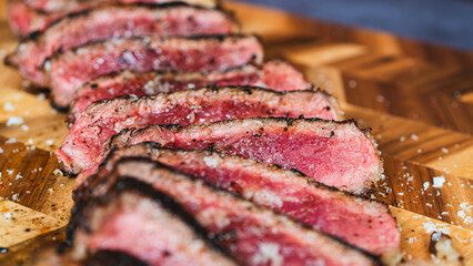 Thick rare smoked sirloin steak, sliced and elegantly arranged on a wooden board with Maldon salt. Beautiful presentation, showcasing a juicy pink interior and caramelized crust. Ideal for gourmet mea