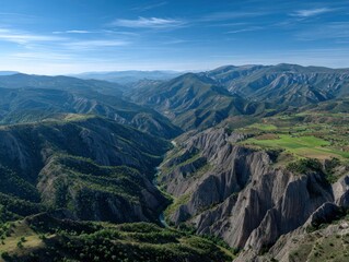 Naklejka premium Vast mountain landscape with grey eroded peaks green valleys a river cutting through the terrain under a clear blue sky