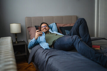 Fototapeta premium Man relaxing in bed looking at phone screen