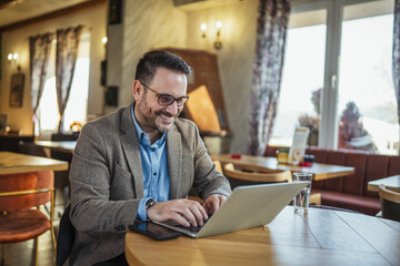 Fototapeta premium Mature businessman working on laptop in cafe smiling happily